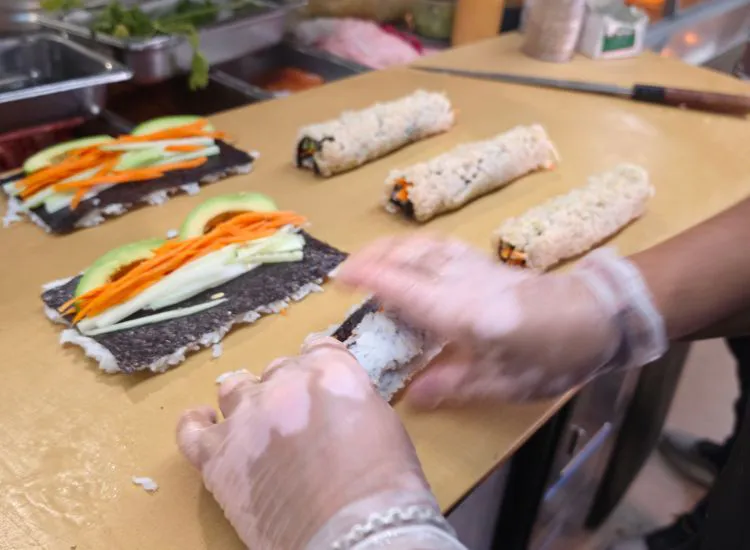 Chef hands rolling fresh sushi rolls at Hashi Sushi counter with nori, rice, and colorful ingredients visible