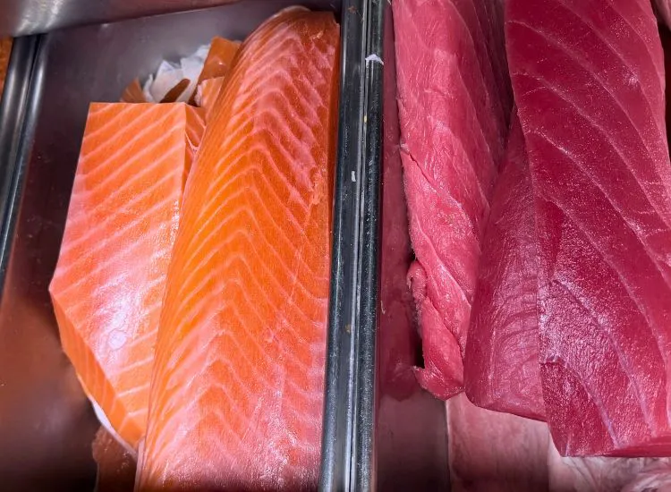 Fresh salmon and tuna fillets displayed in a refrigerated case at Hashi Sushi, showing vibrant orange and deep red fish re...