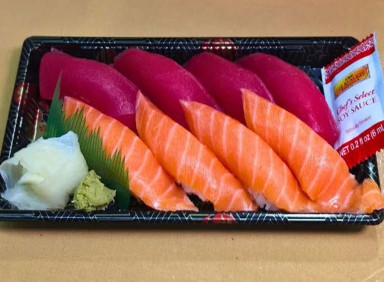 Four pieces of nigiri sushi with magenta topping and orange salmon, served on black tray with wasabi and pickled ginger