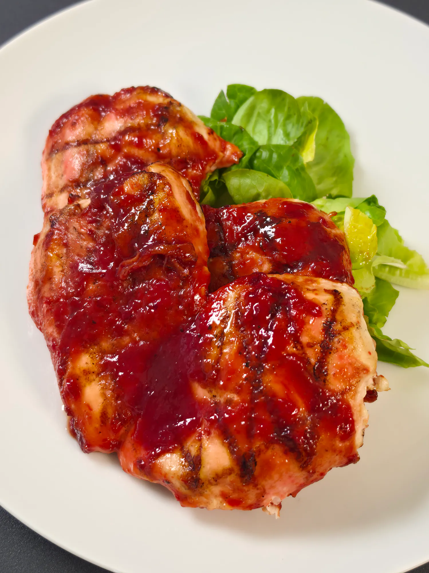 Grilled chicken pieces generously coated in cherry BBQ sauce, served with fresh green lettuce.